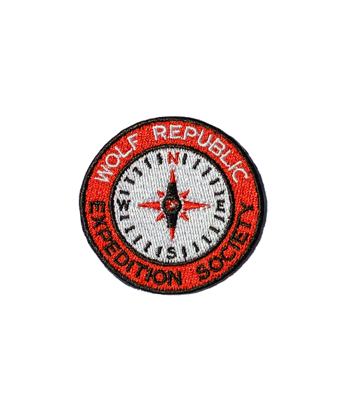 A red and white embroidered patch for dogs in the shape of a circle compass that reads Wolf Republic Expedition Society