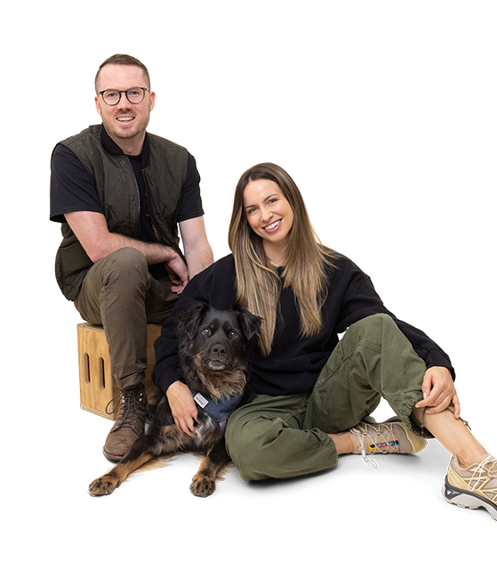 The two founders of Wolf Republic are sitting with their black rescue dog sitting in between them while smiling