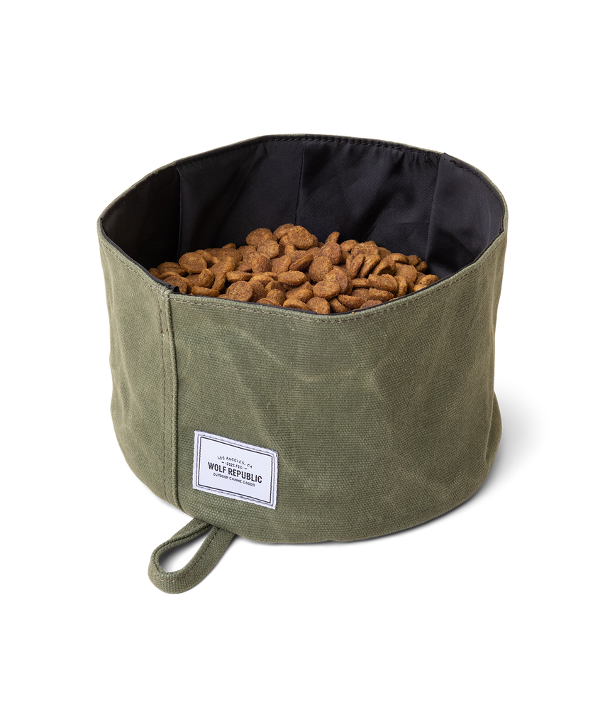 A green waxed canvas waterproof collapsible dog bowl is filled with dog food