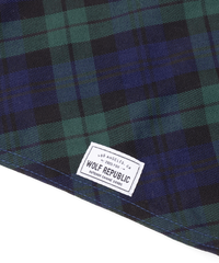 a close up photo of a navy and green plaid fabric swatch with a logo woven label in white attached